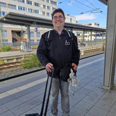 Andreas Unkelbach am Bahnhof in Giessen mit Koffer und Tasche, daran ist Gideon ein gehaekelter Gargoyle gebunden